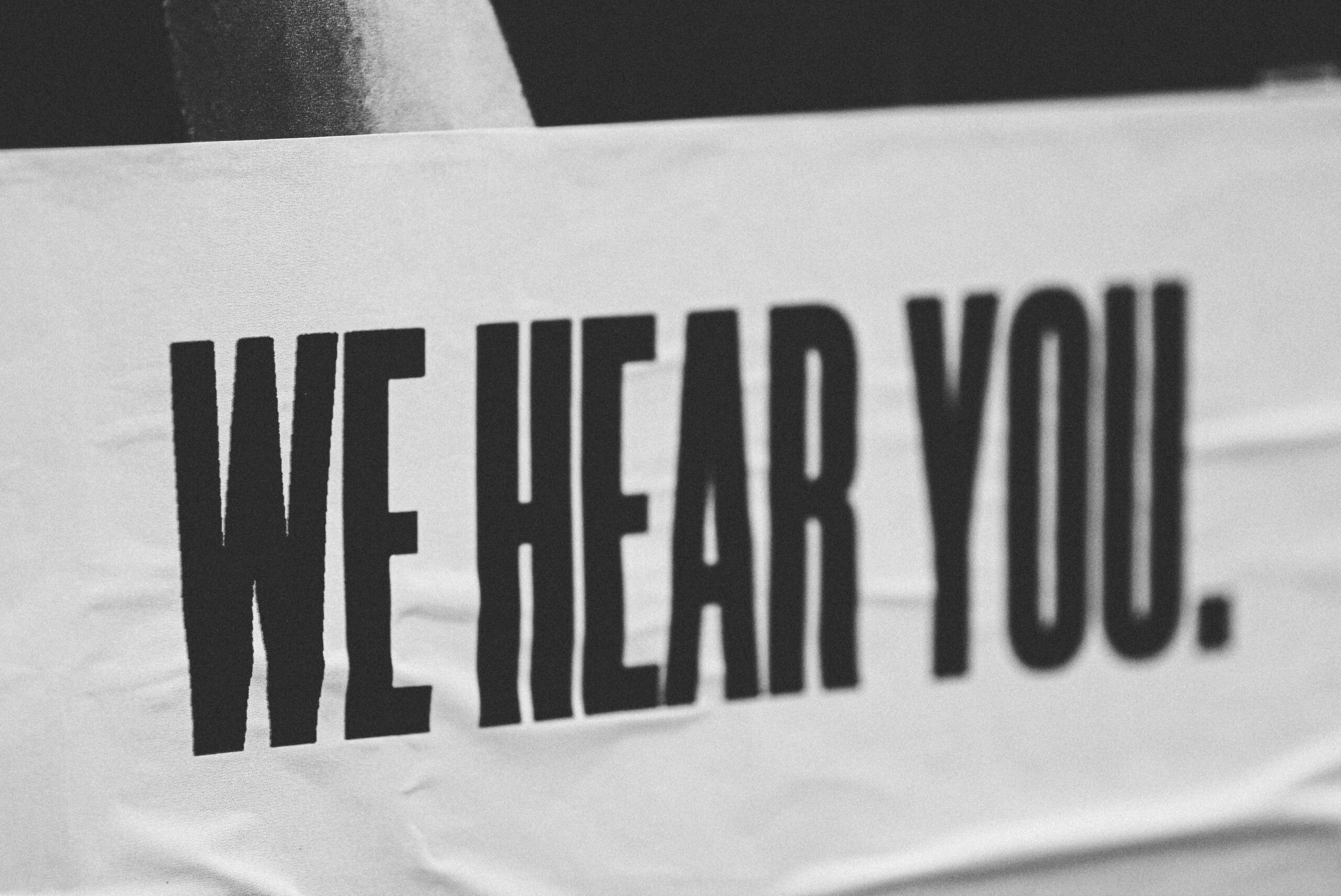 Close-up of a monochrome banner with bold text reading “WE HEAR YOU.” printed on it.
