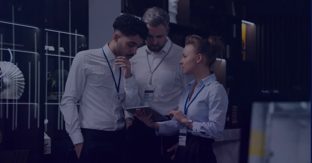 Team collaboration on business strategy, with one person holding a tablet while discussing insights in a corporate environment.