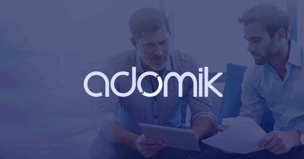 Two young contemporary elegant businessmen discussing terms of new deal , enhanced by Adomik logo on the front