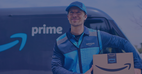 Amazon Prime delivery driver in a blue uniform holding a Prime box beside a Prime van.
