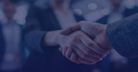 Two people shaking hands in a blurred business setting, signaling a deal or partnership.