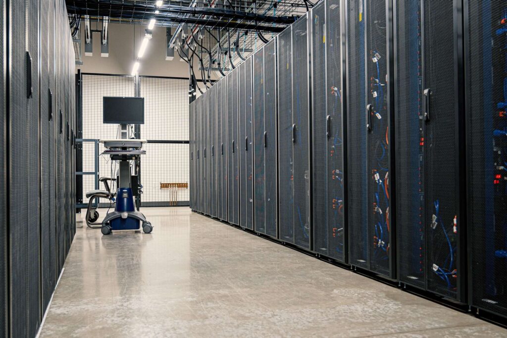 Data center aisle with tall server racks on both sides and a monitor on a mobile cart in the center.