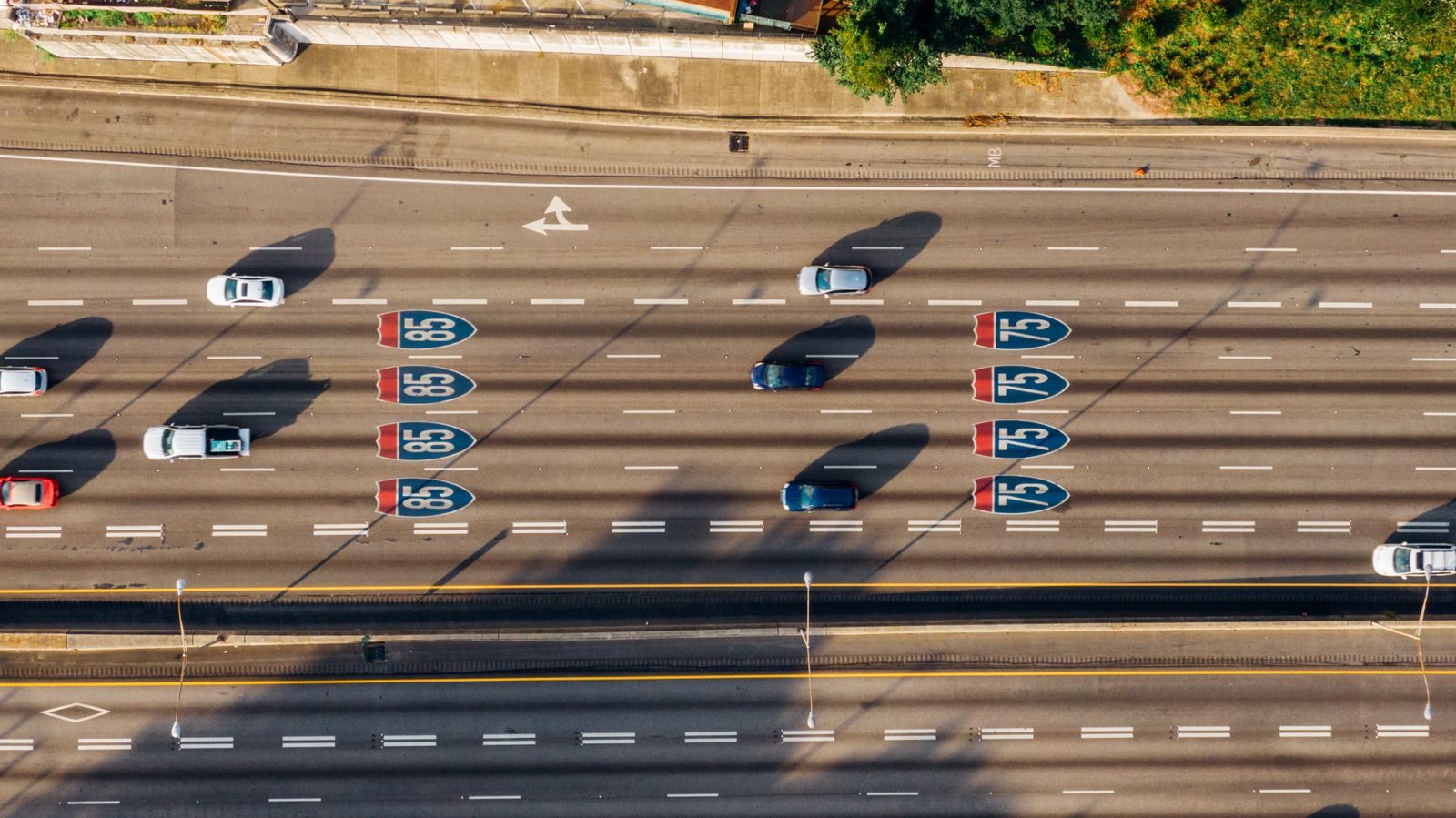 Aerial view of a multi-lane highway with cars and I-80 and I-75 shields on the road; long shadows from structures cross the lanes.