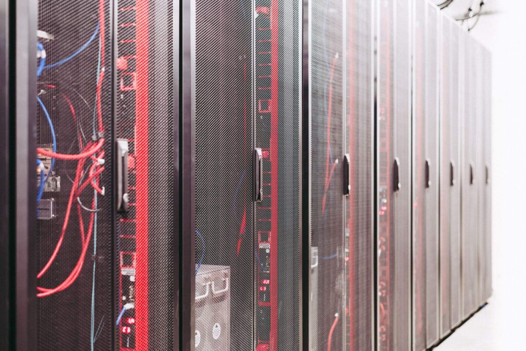 Row of dark server racks with red indicator lights and blue cables in a data center corridor