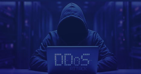 Hooded figure typing at a laptop in a blue-toned data center, screen displaying 'DDoS ATTACK'.