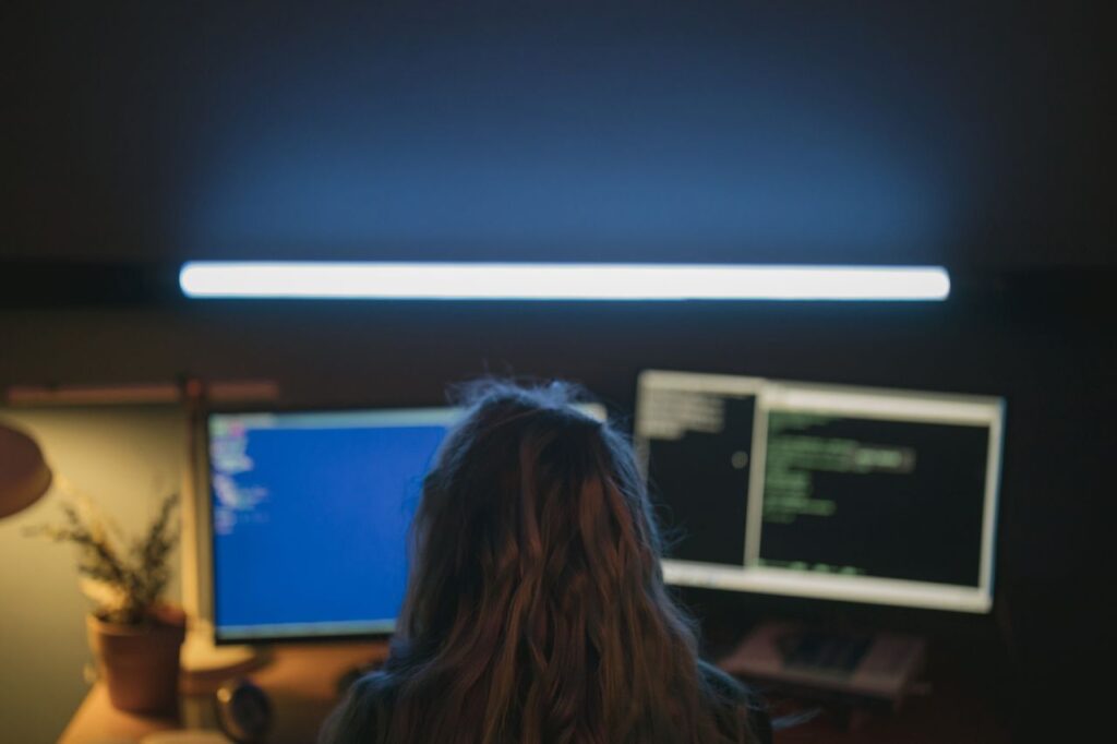 An engineer working at two monitors of code in a dim room
